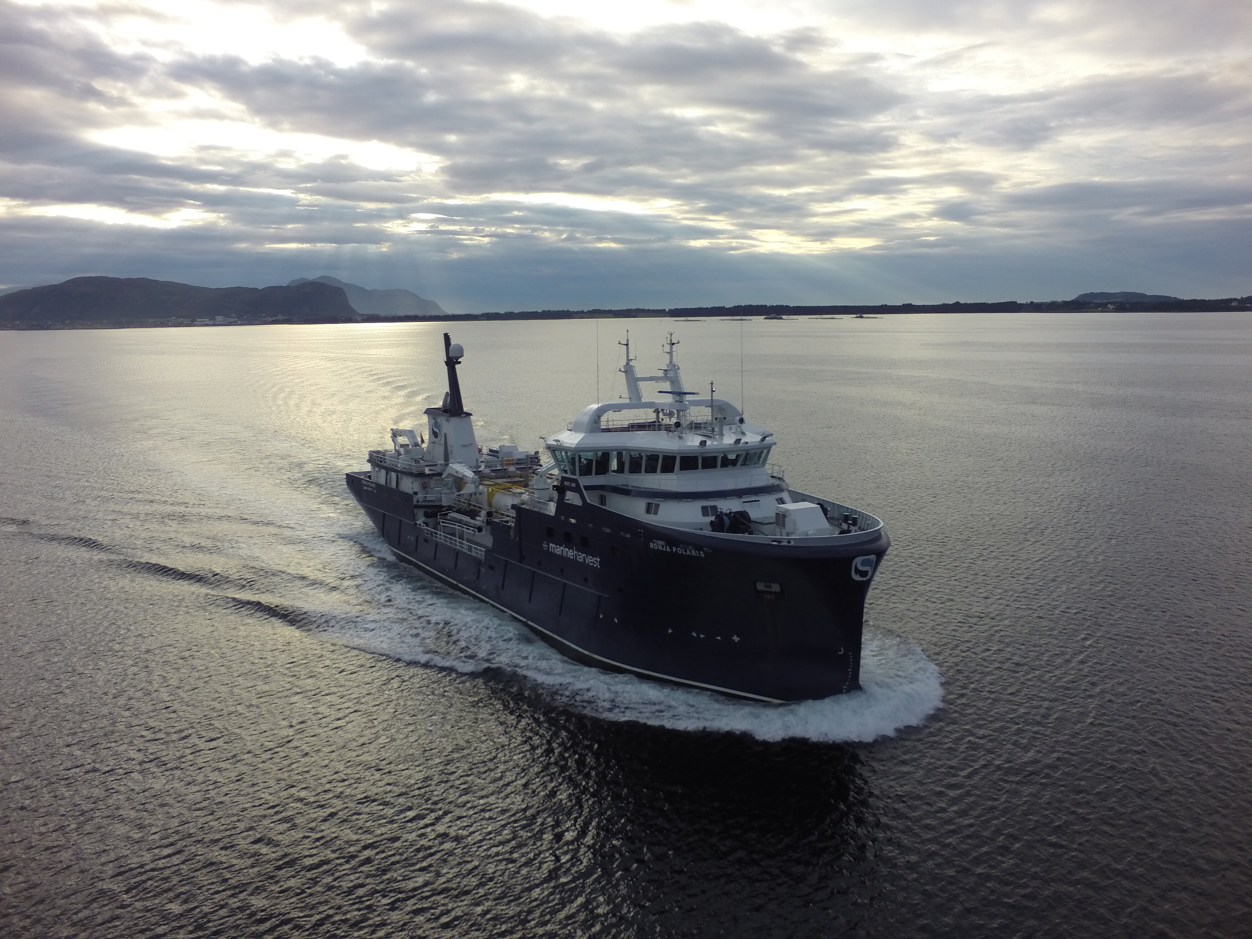 Båten Ronja Polaris på veg med laks nordover kysten fra Ålesund med Valderøy og Vigra i Giske kommune i bakgrunnen
